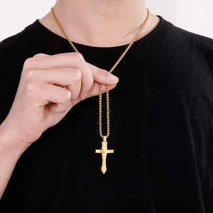 Gros plan d'un collier avec pendentif croix dorée porté sur un tee-shirt noir