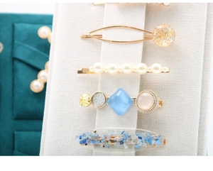 Macro shot of 5pcs gold alloy hair clips with pearls and blue resin on white display stand