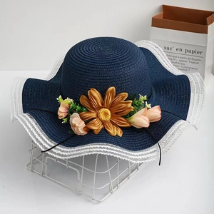 Detail of navy blue straw sun hat with large sunflower and lace brim on a table