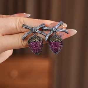 Macro shot of bow strawberry earrings with pink and yellow zircons in black gold
