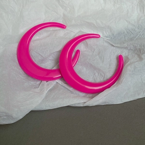 Detail view of oversized neon pink resin C-shaped hoop earrings on textured white paper