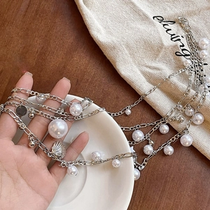 Detail of layered waist chain with pearls and shell pendant held over a ceramic saucer