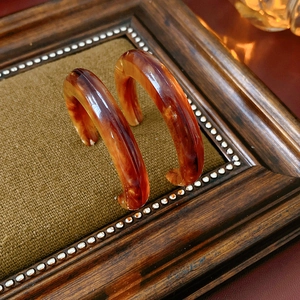 Detail view of brown tortoiseshell resin C-shaped earrings on vintage wooden tray