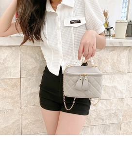 Detail of light gray quilted mini bag with pearl handle and golden chain on marble