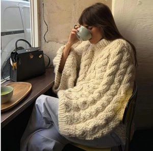 Detailed knit texture of cream-colored cable knit sweater in a cozy cafe setting