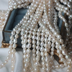 Lustrous white irregular baroque pearls draped over a blue velvet box with satin background