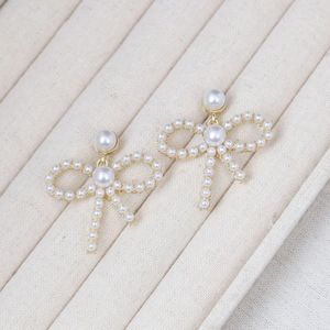 Detailed view of bowknot pearl earrings with gold base on a textured jewelry display tray