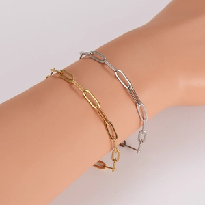 Detail showing gold and silver paperclip chain anklets worn on wrist with metallic shine