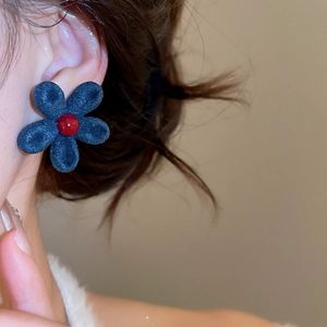 Detailed close-up of a navy blue flocked flower earring with a deep red center on a model