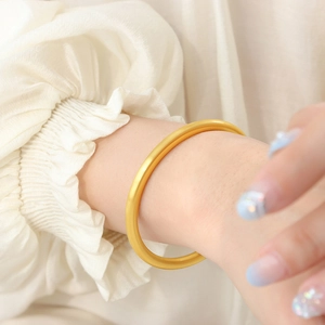 Minimalist matte gold geometric bangle for women shown on a model wrist against fabric