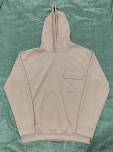 Detail of warm beige hoodie showing the square flap chest pocket and ribbed cuffs finish