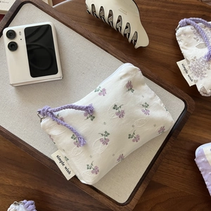Floral cotton coin purse with purple flower patterns and a woven zipper pull on wood