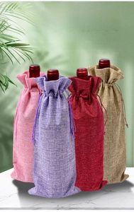 Linen drawstring wine gift bags in four colors on marble surface with green leaves