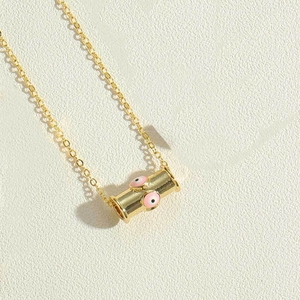Macro shot of gold cylinder pendant necklace with pink and black evil eye design