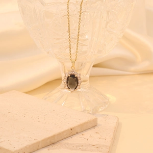 Close-up of a gold oval pendant necklace with a dark gemstone on beige silk and stone
