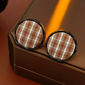 Detail of round fabric checkered earrings with brown plaid pattern and black border trim