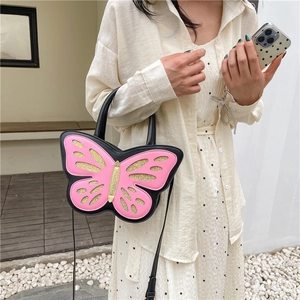 Pink butterfly-shaped handbag with gold glitter wings and black straps on a female model