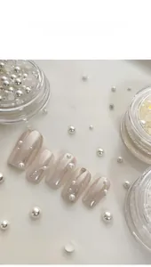 Detailed view of mixed size white half pearls applied on glossy nude manicure nails