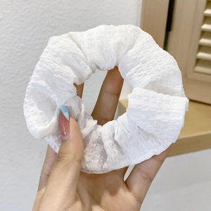 Close-up of white pleated fabric scrunchie being held, showing soft texture and elastic detail