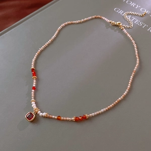 Detail of beaded necklace featuring red gemstone pendant and white pearls on vintage book