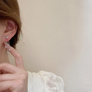 Elegant silver tassel earrings with metallic beads on model against cream background