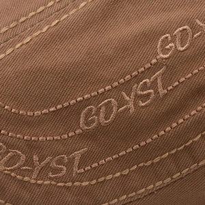 Detailed macro view of GDYST embroidery on premium brown twill canvas flat cap fabric