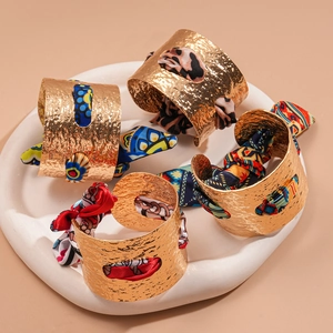 Bracciali rigidi dorati martellati con sciarpe di seta colorate e motivi geometrici