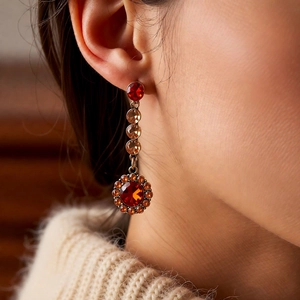 Détail de boucles d'oreilles vintage avec des strass ronds rouges et ambrés