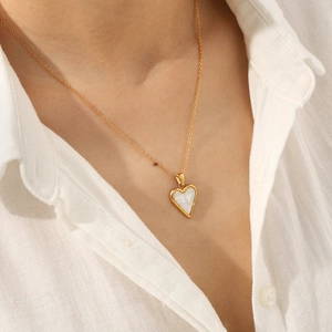 Gold heart pendant necklace with white shell inlay worn by a model on white shirt
