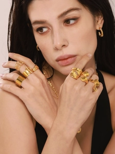 Close-up of stacked 18K gold-plated rings and C-shaped earrings worn by a model
