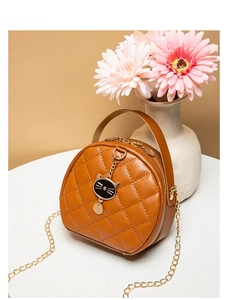 Detail of a brown quilted round bag featuring a gold chain and black cat charm