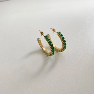 Detailed macro shot of gold hoop earrings set with emerald-cut green zircon stones