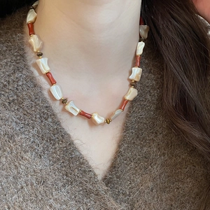 Detailed view of irregular shell beads and red stone beads on a gold-accented necklace