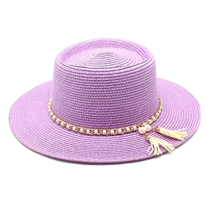 Détail d'un chapeau de paille violet orné d'une chaîne dorée et de pompons blanc cassé