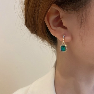 Close-up of emerald green square earrings with halo diamonds and 18K gold plating