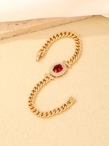 Close-up of golden cuban chain bracelet featuring a red oval stone with CZ inlay