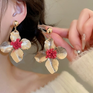Close-up of a large gold flower earring with red center worn by a female model