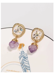 Macro detail of Bohemian gold earrings with purple natural stone and shell inlay