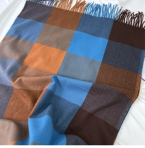 Detailed flat lay of plaid cashmere scarf with orange and blue tassels on white fabric