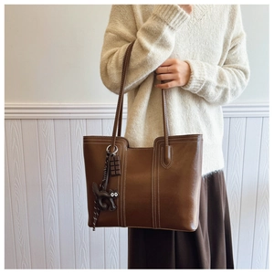 Detail of dark brown tote bag with white contrast stitching and cat charms on handles