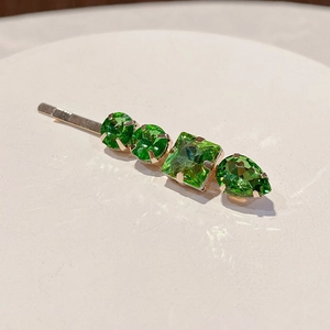 Macro detail of gold hair clip featuring four emerald green crystals in claw setting