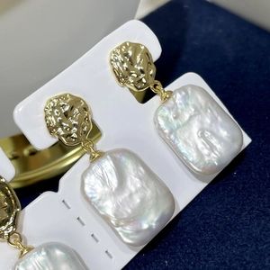 Detail of baroque pearl earrings with golden lava texture on elegant white display stand