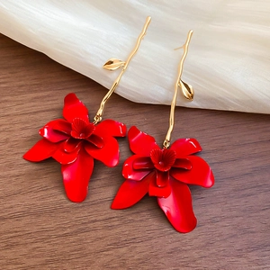 Macro shot of long red flower drop earrings with golden leaf hooks on a wooden surface