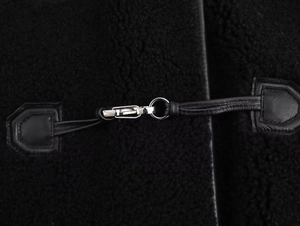 Détail macro de la boucle en métal argenté et texture en peau lainée noire de la veste
