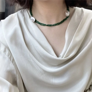 Detail of dark green multi-strand beaded necklace with baroque pearls on model