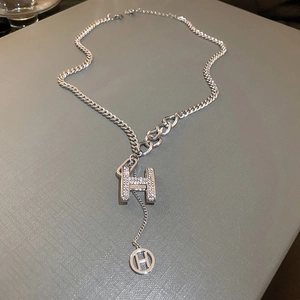 Close-up of silver-tone chain necklace with diamond-encrusted letter H and hollow charm