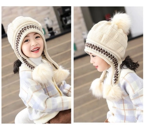 Dettaglio del cappello in maglia color crema per bambini con paraorecchie e morbidi pompon
