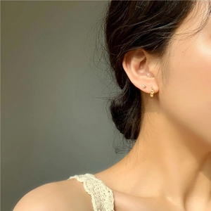Close-up of a model wearing a gold minimalist spherical stud and textured hoop earring