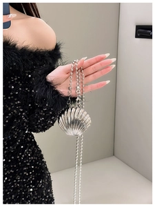 Close-up of a silver shell-shaped mini bag with a beaded chain held by a model