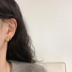 Close-up of minimalist gold oval stud earrings and hoop set worn on model ear